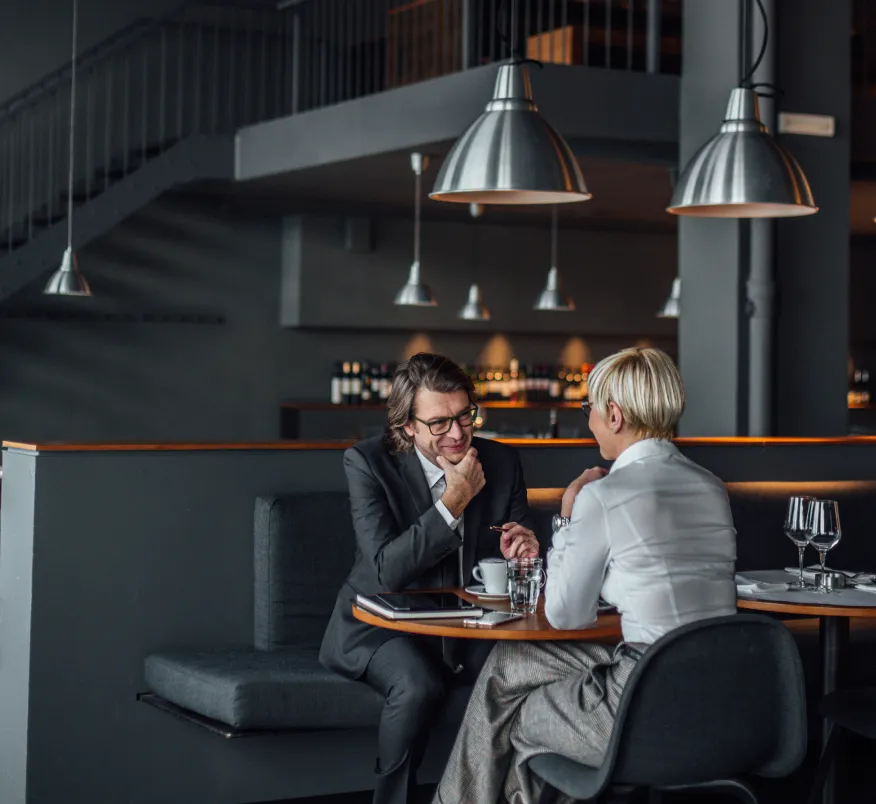 Professional man and woman in business attire talking at a sleek, upscale restaurant booth