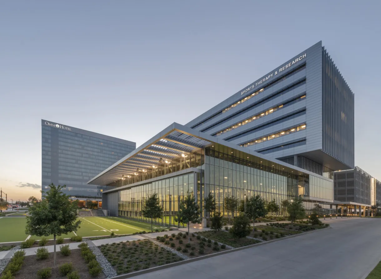 Modern sports therapy and research facility with glass facade and adjacent green athletic training field.